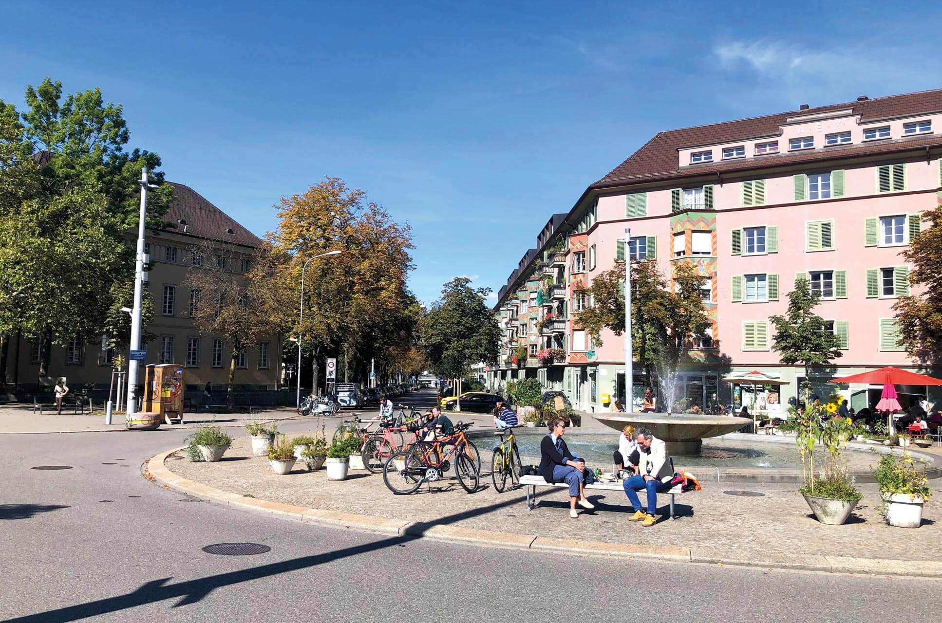 Personen sitzen neben ihren Velos auf Bänken um den Brunnen am Bullingerplatz.